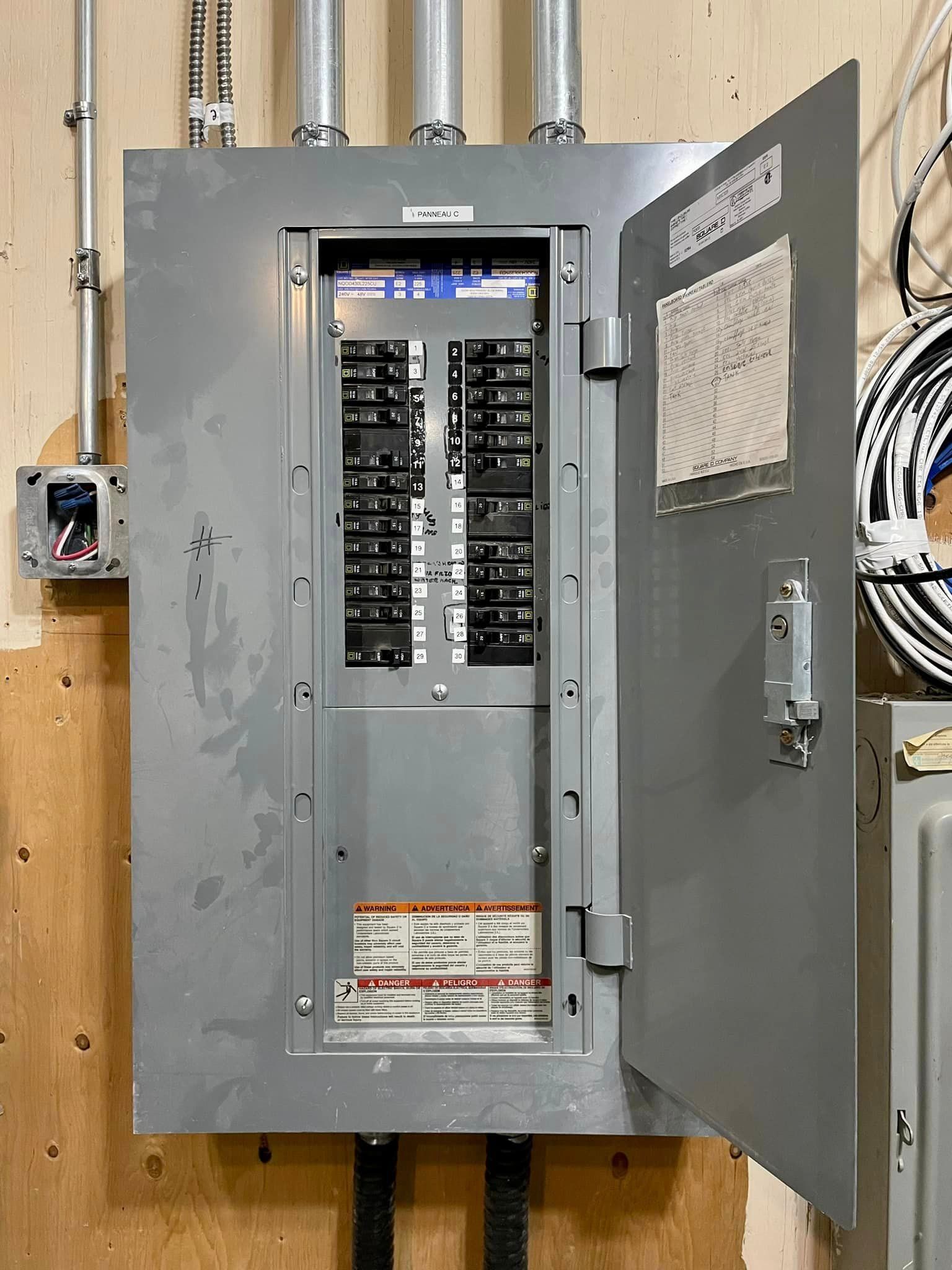 Opened electrical panel on a wooden wall. Gray panel with rows of black circuit breakers.