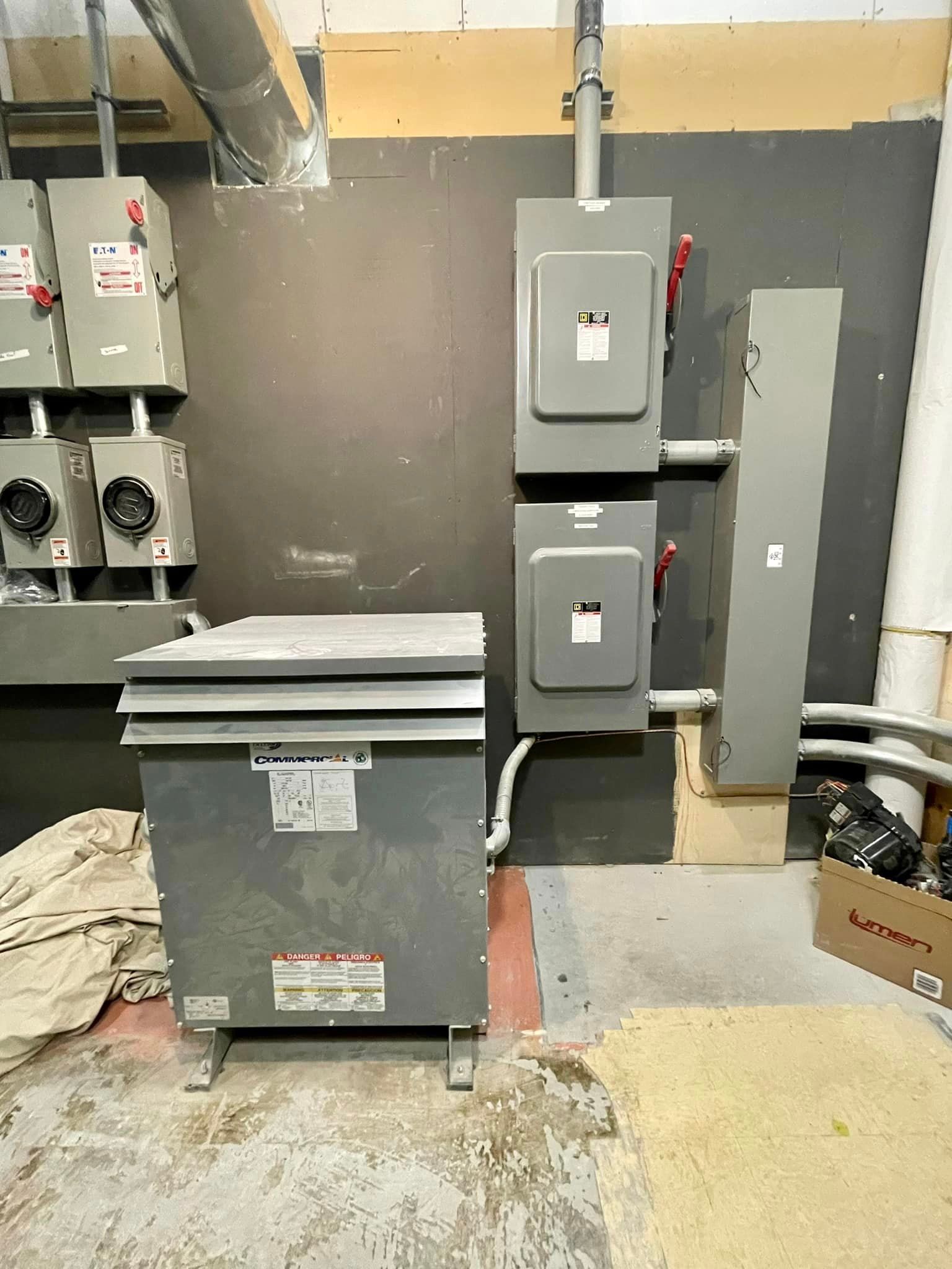 Electrical equipment, including a transformer, breaker boxes, and conduit in a utility room.