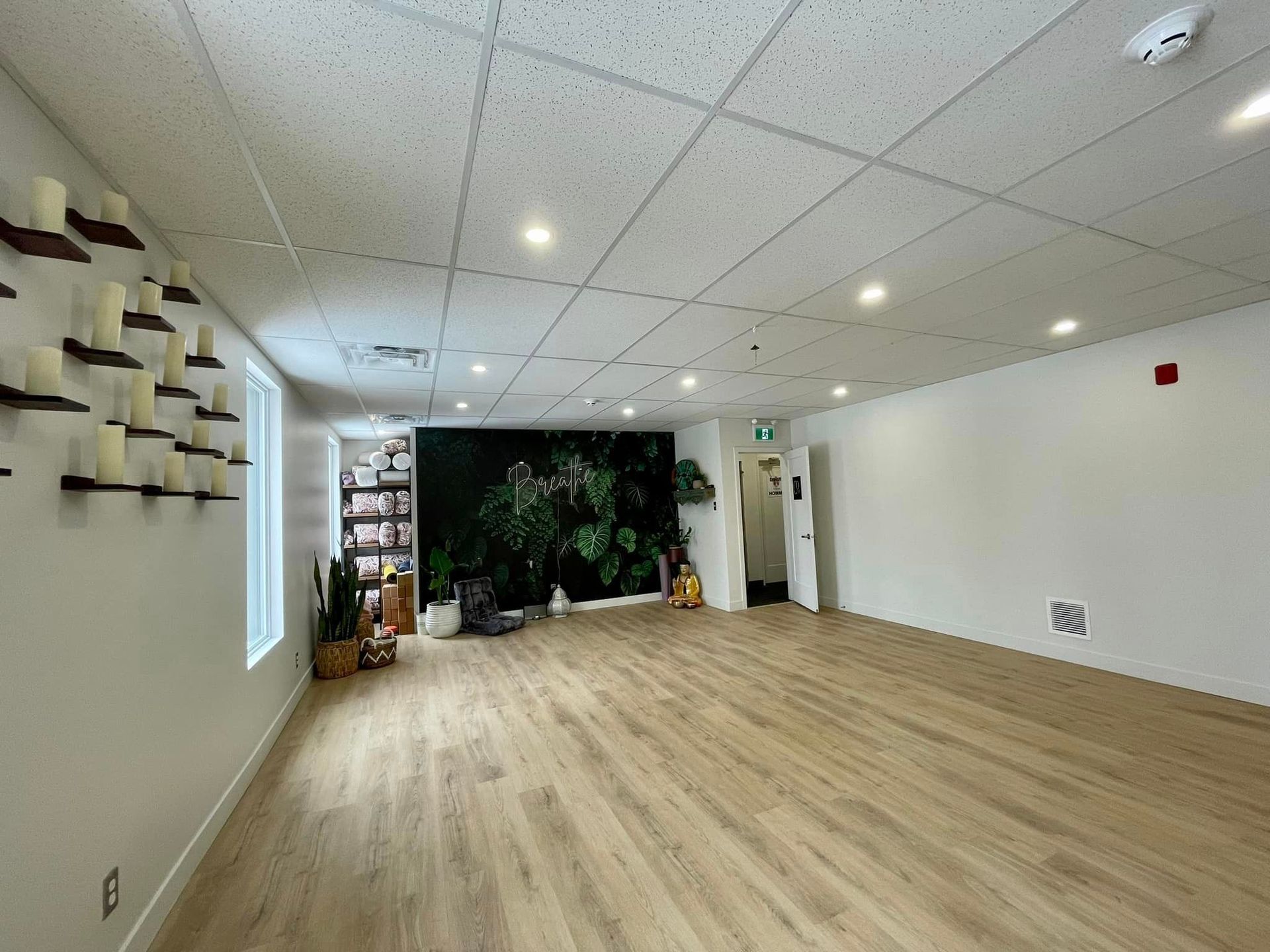 Empty yoga studio with wooden floor, white walls, candles, and a large plant mural.
