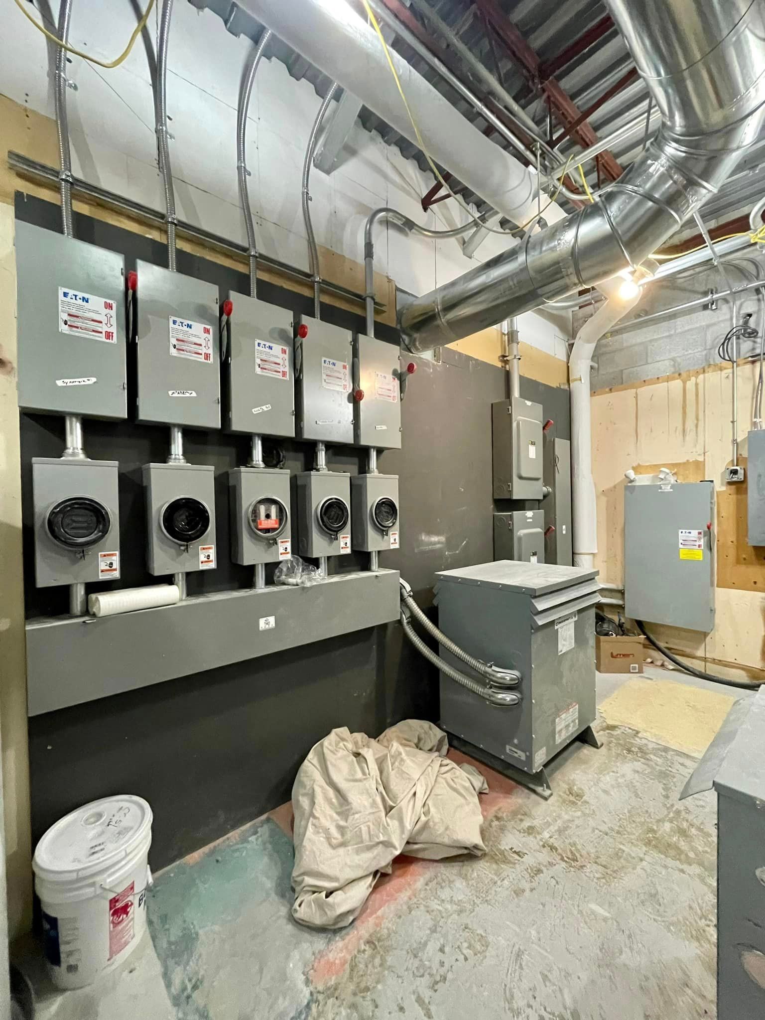 Electrical panels and transformer in a construction setting with exposed wiring and ductwork.