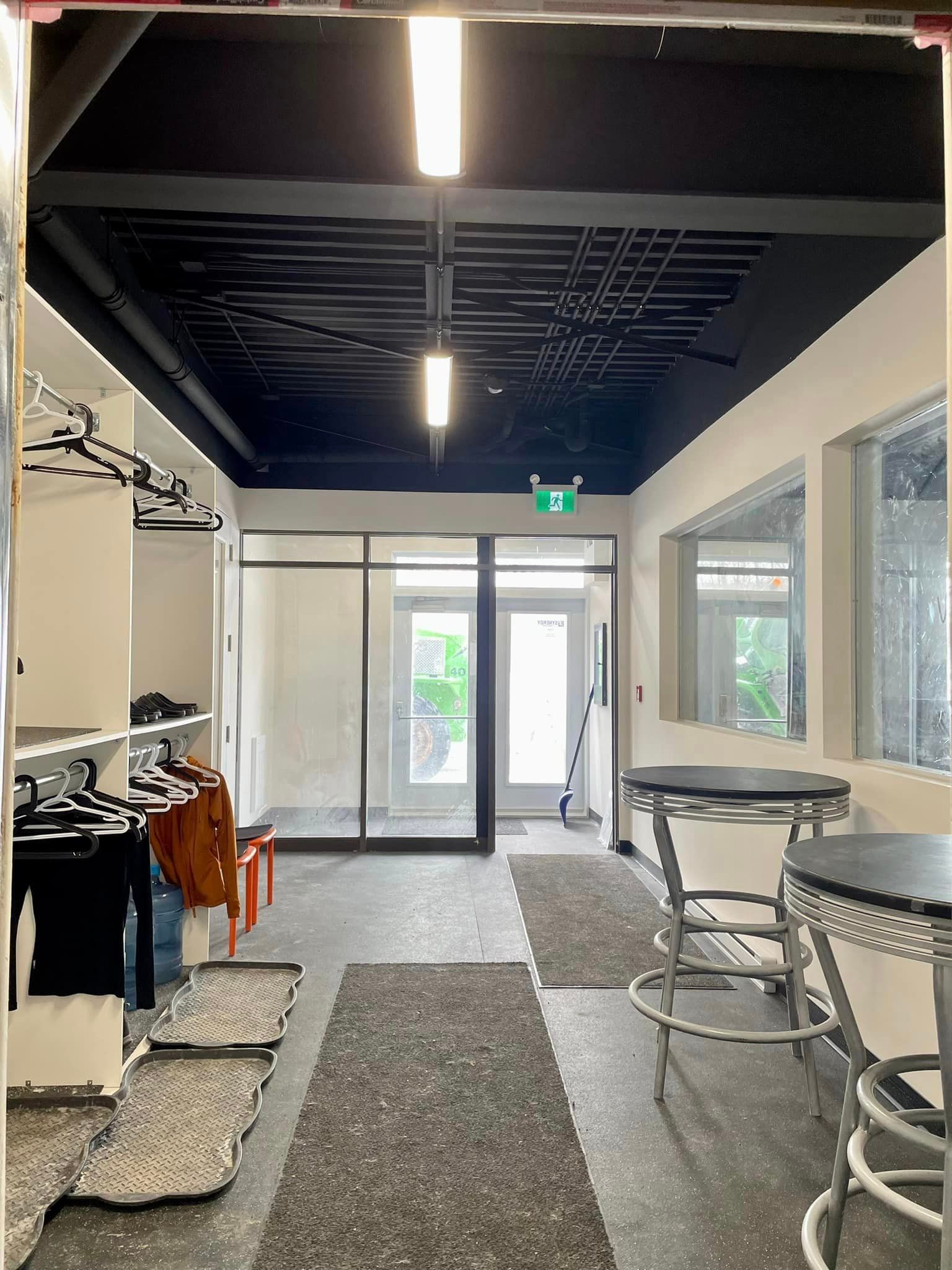 Interior hallway with black ceiling, metal stools, coat rack, and glass doors leading outside.