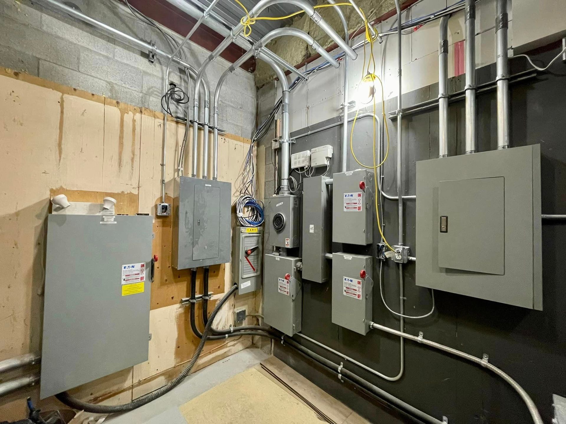 Electrical equipment and conduits on a wall in a utility room. Gray metal boxes and silver pipes against a wall.