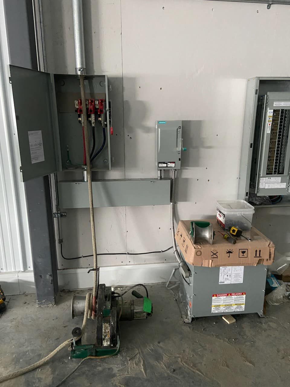 Electrical panel, wiring, and equipment installed on a wall in a construction setting.