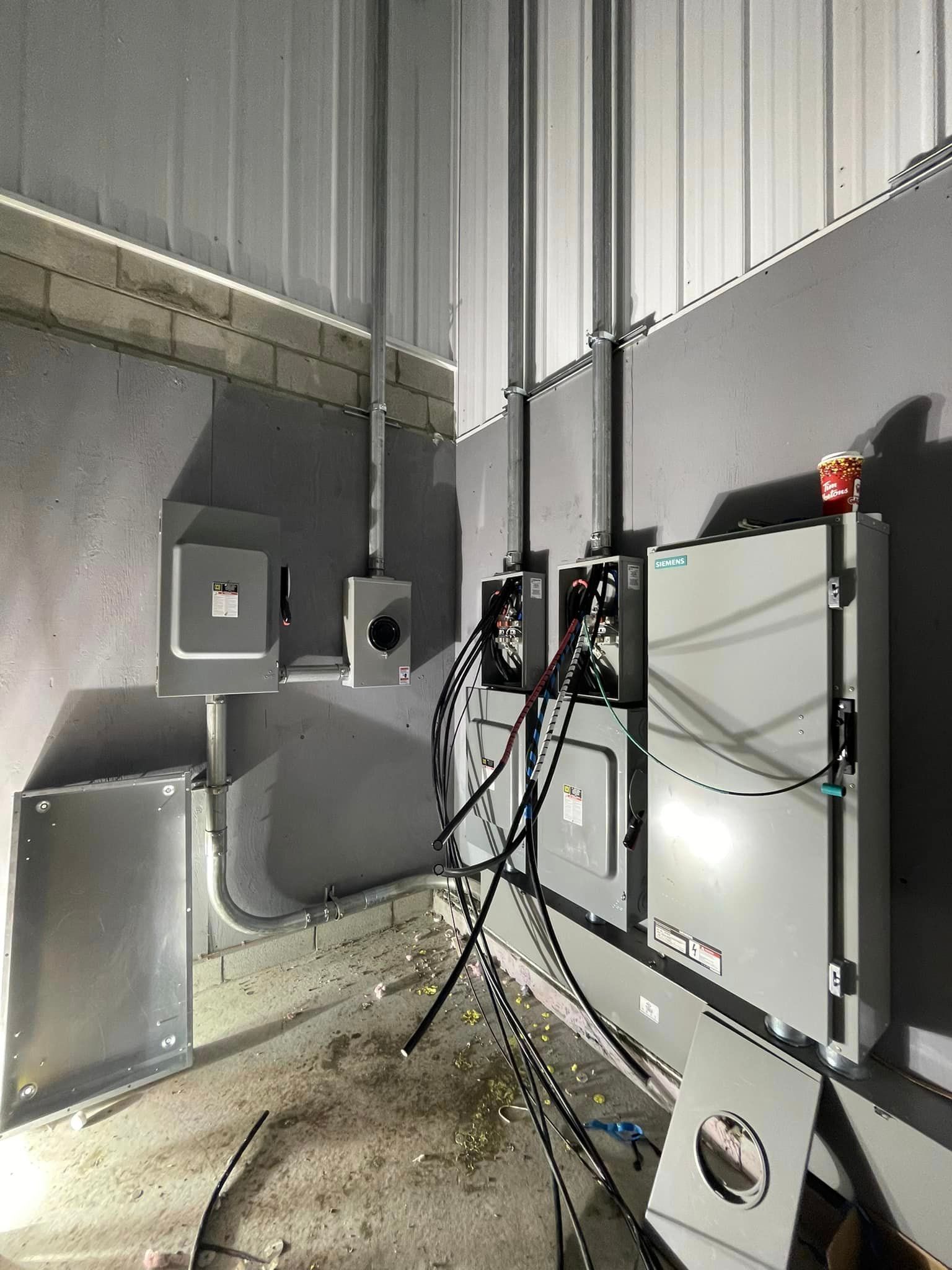 Electrical wiring and panels installed on a gray wall in a metal-walled room.