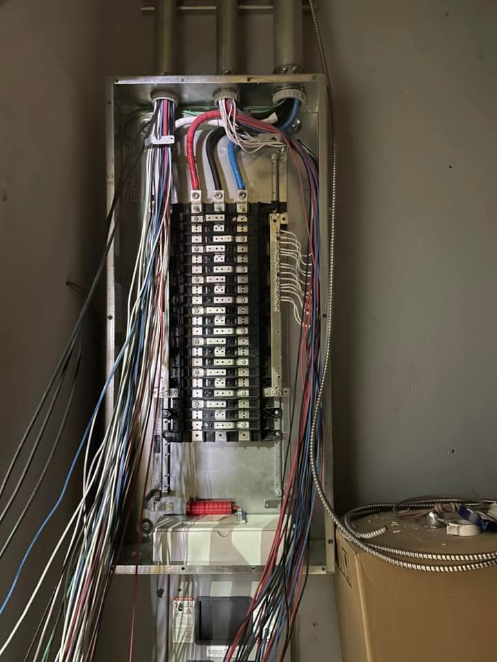Electrical panel with many wires protruding, set in a gray enclosure against a concrete wall.