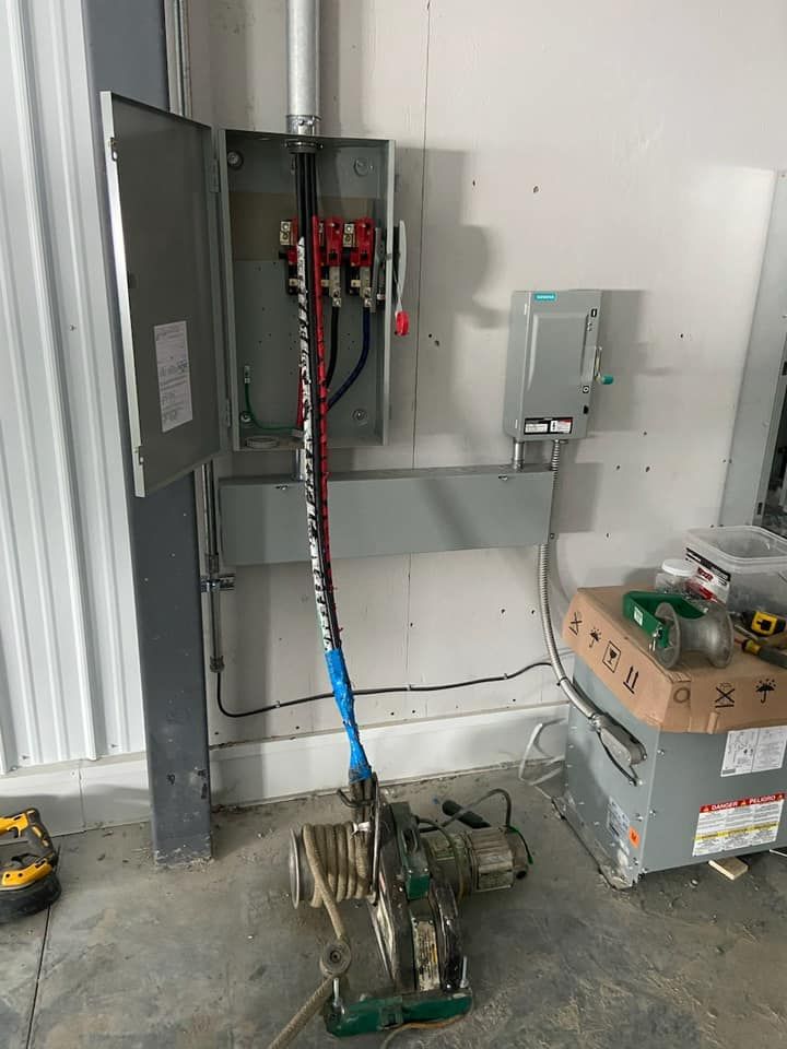 Electrical panel with exposed wires, conduit, and attached saw on a concrete floor.