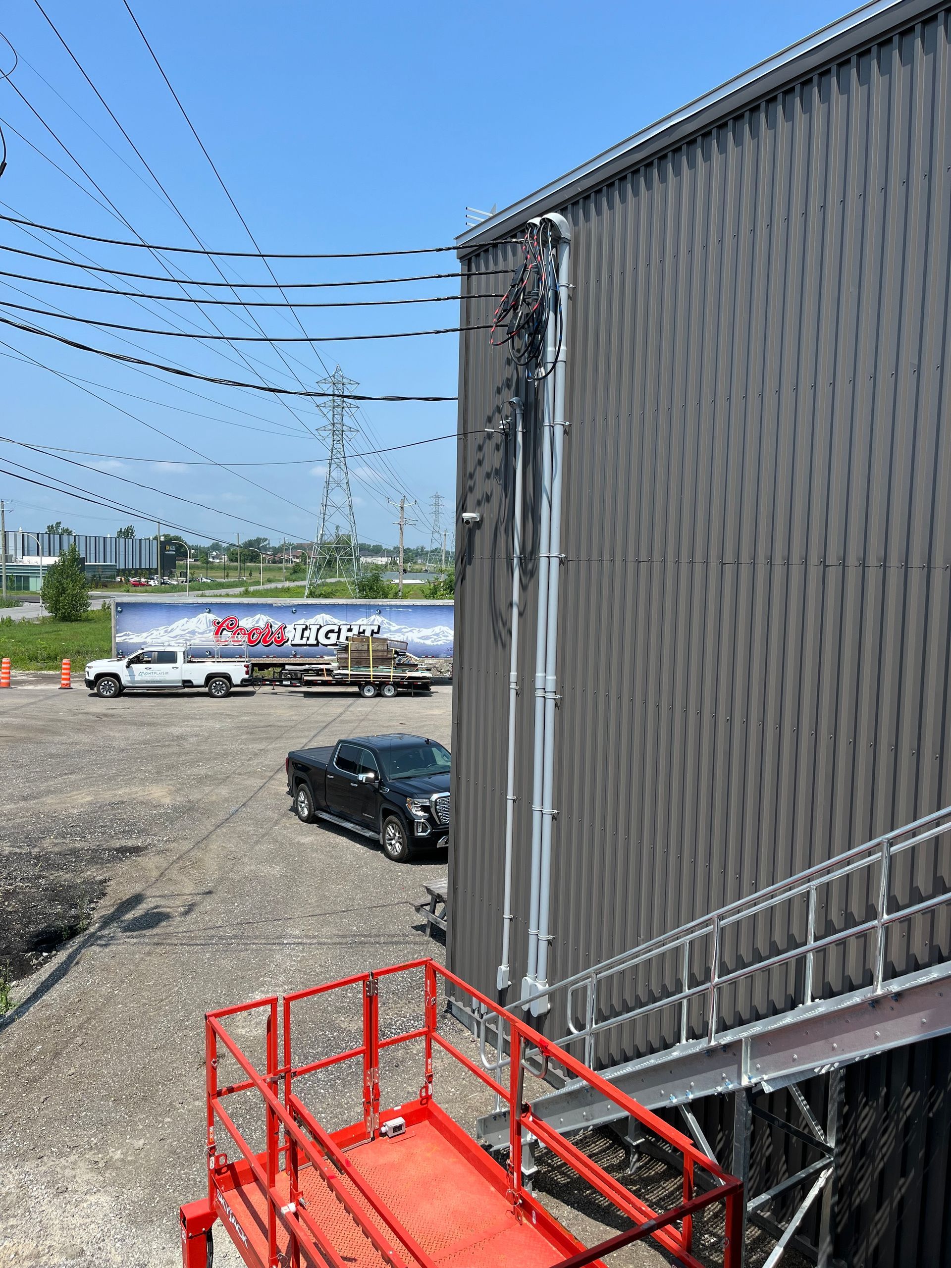 Metal building with power lines overhead, a black truck, and a red work platform.