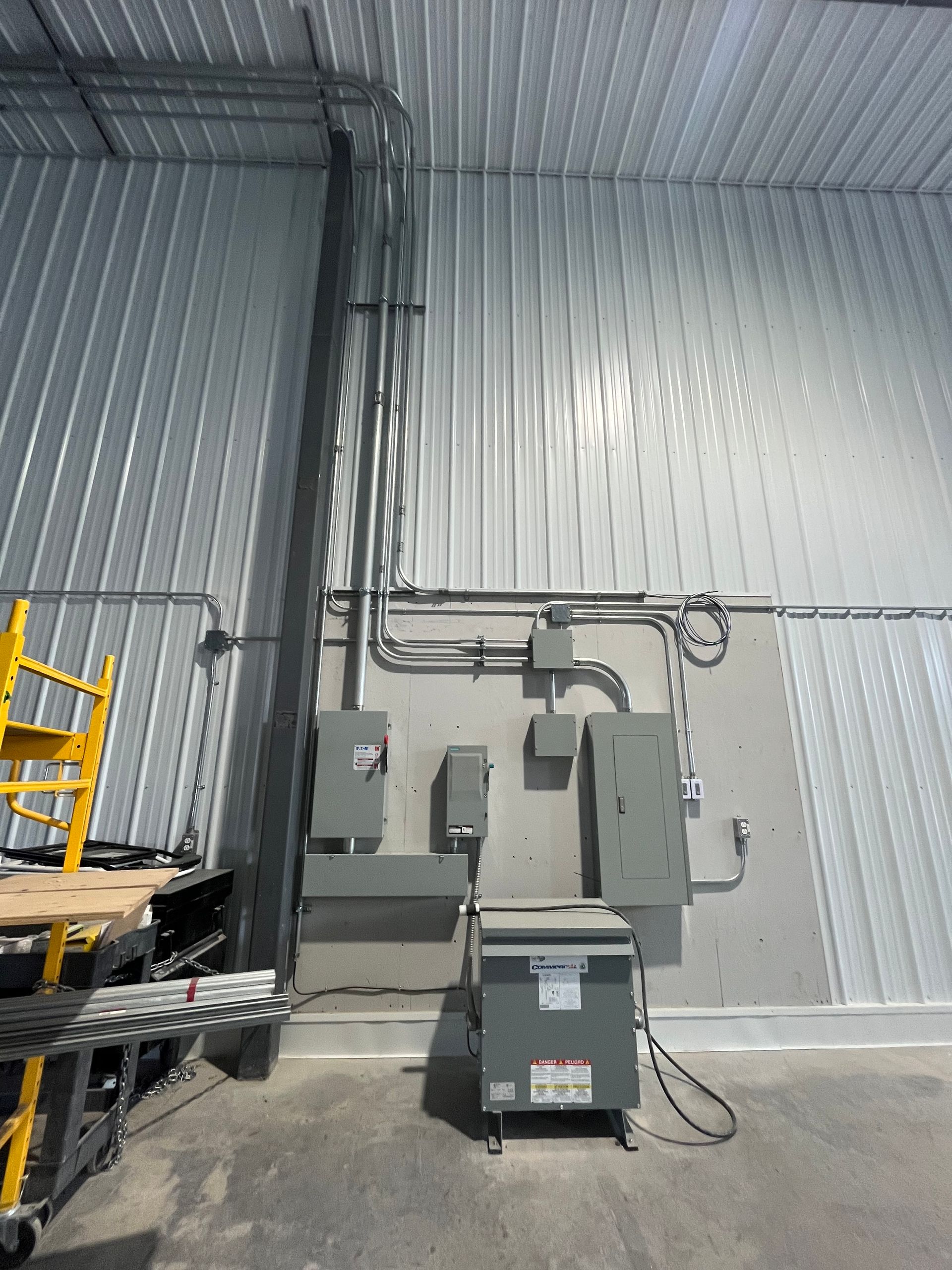 Electrical panel and conduit installation on a gray metal wall inside a building.