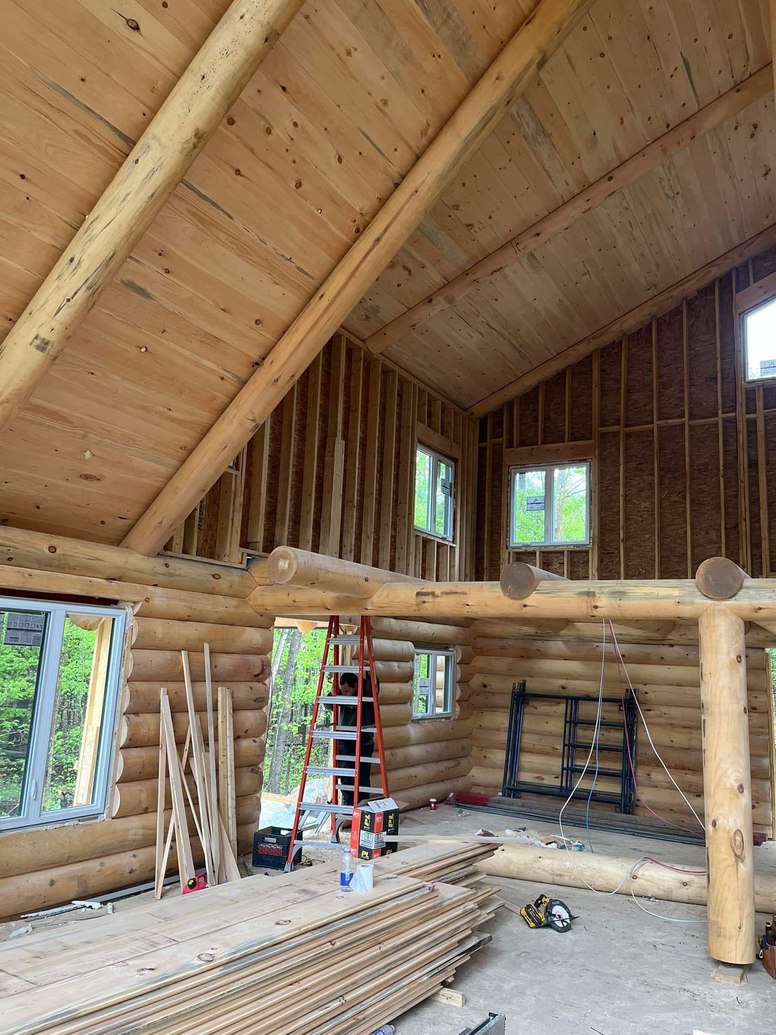 Interior view of a log cabin under construction with exposed wooden beams, roof, and walls.