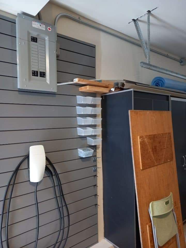 Electrical panel and EV charger on a gray wall in a garage, next to storage cabinets.