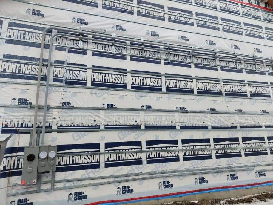 Electrical conduit and junction boxes installed on a building's exterior, over a membrane with printed text.