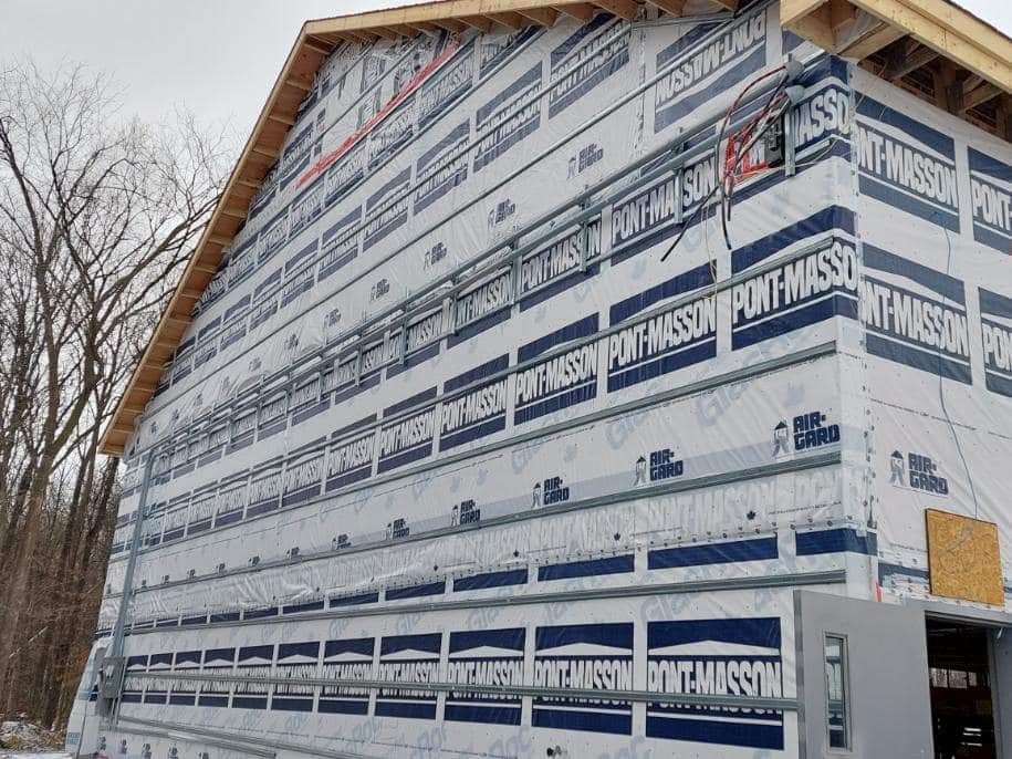 Exterior wall of a building with blue and white wrap, metal supports, and electrical components.