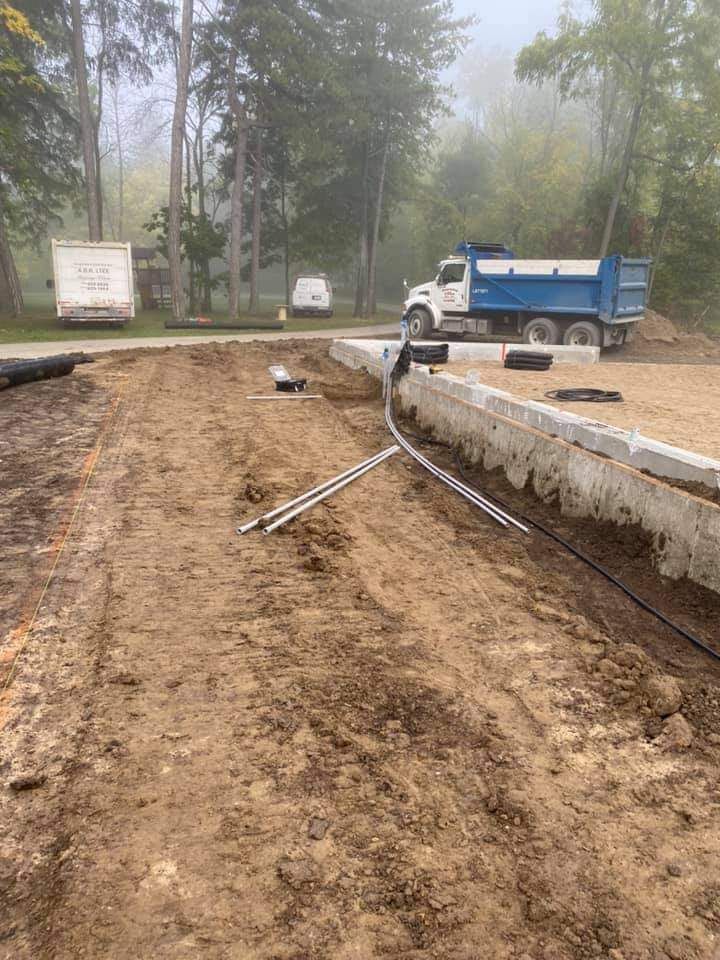 Dirt construction site with concrete foundation, utility pipes, and a dump truck under a hazy sky.
