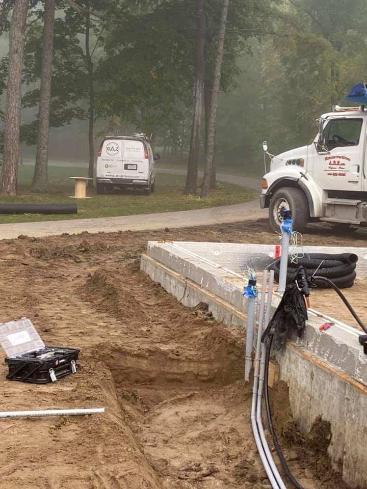 Construction site with a truck, van, and foundation being worked on, in a natural setting.
