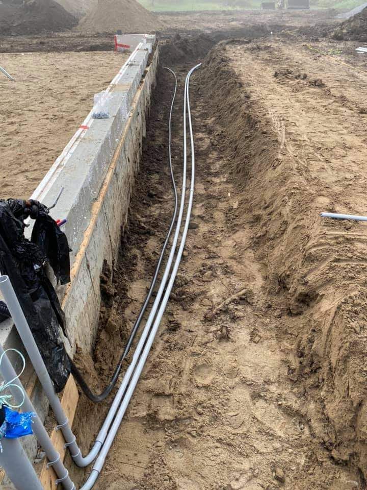 Trench with gray electrical conduits running alongside a concrete foundation, likely for wiring.