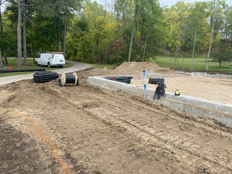 Construction site with gravel foundation, dirt, utility cables, and a white work van in the background.
