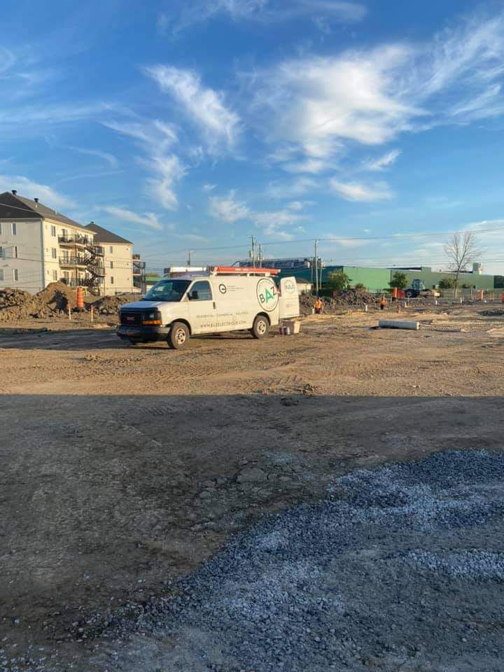 White service van on a construction site with buildings in the background under a blue sky.