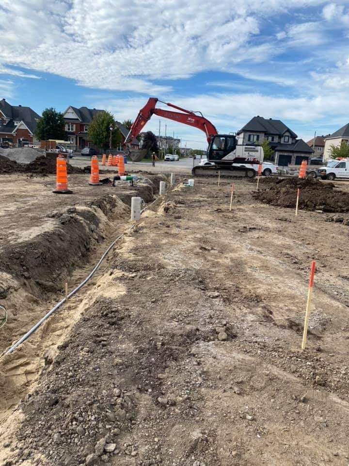 Construction site with a large excavator, trenches, and orange safety cones.