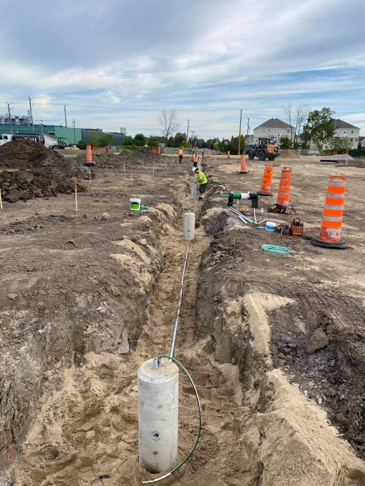 Construction site with trench, concrete posts, workers, and safety cones.