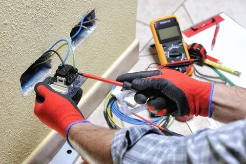 Un électricien travaille sur une prise électrique avec un tournevis.