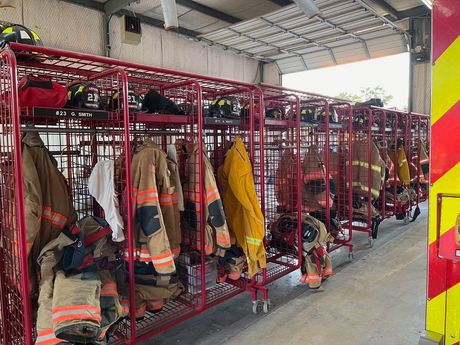 A row of red lockers filled with firefighter 's uniforms and helmets.