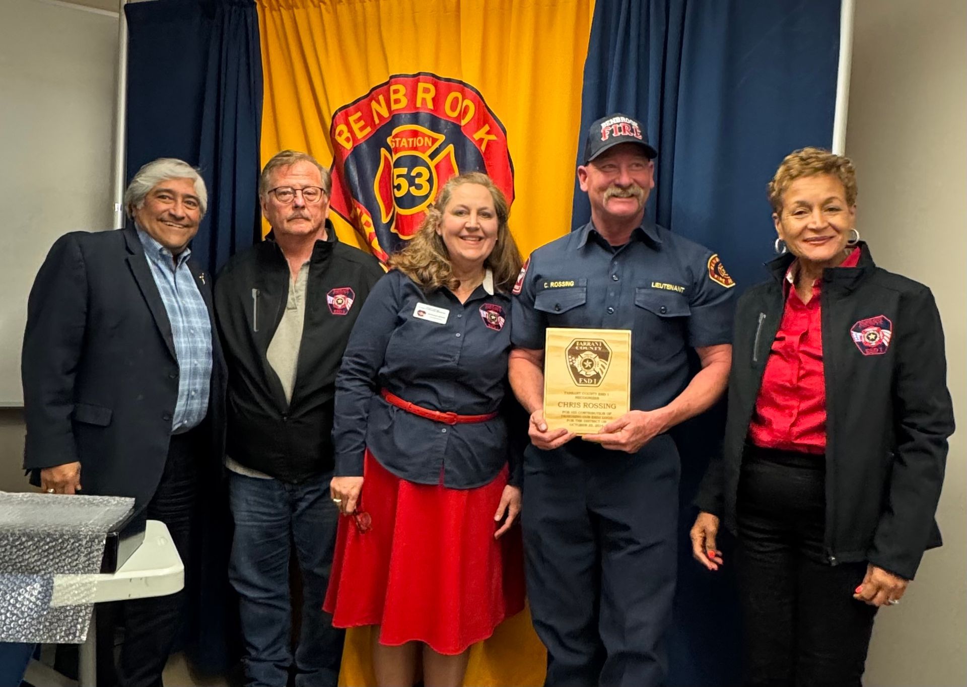 A group of people are posing for a picture in front of a fire department flag.