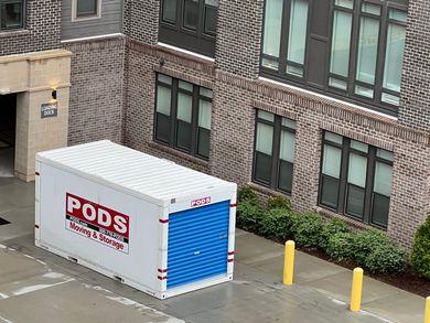 White PODS storage container with blue door beside a brick building and yellow bollards