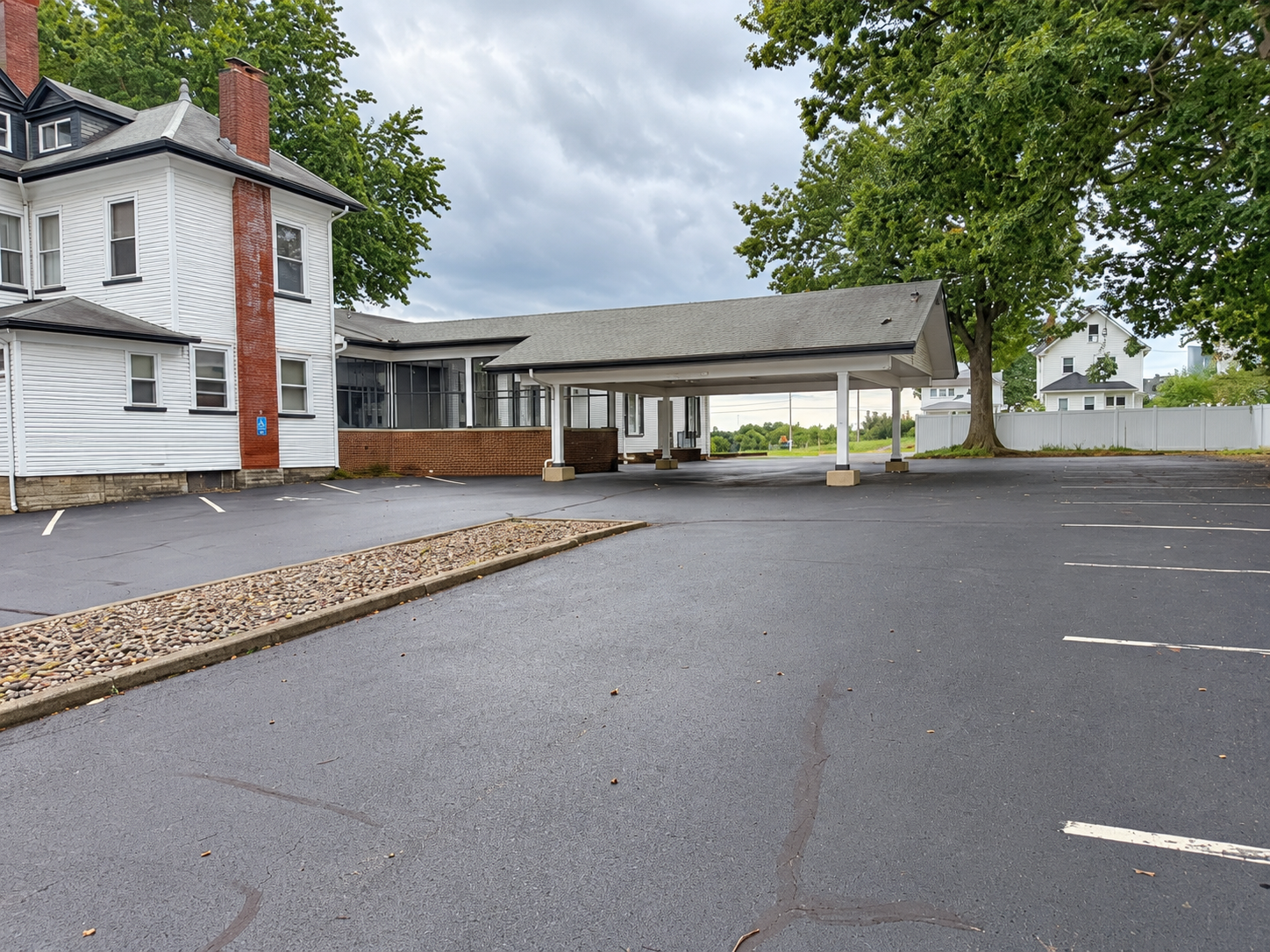 Empty parking lot beside a white building and covered drive-through canopy on a cloudy day