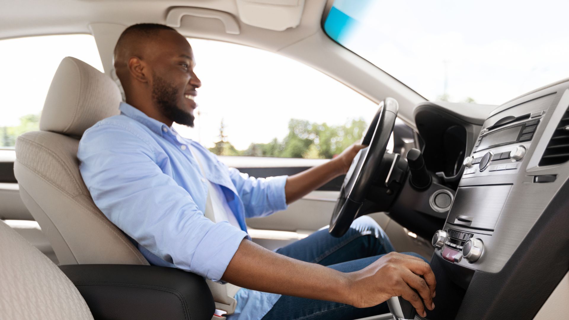 Driver in a blue shirt seated in a car, adjusting controls on the center console.
