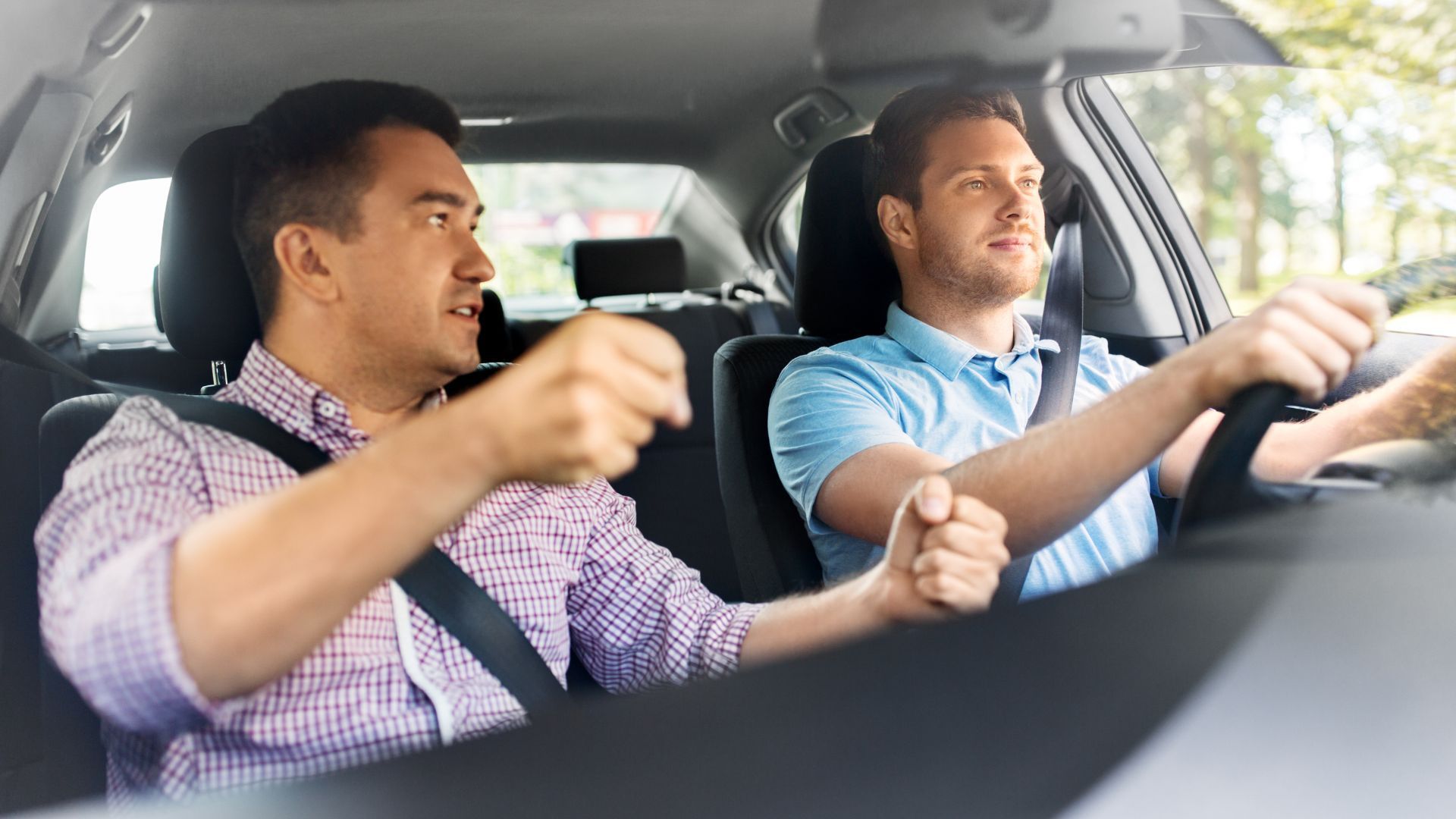 Two men in a car, one in the passenger seat gesturing while the driver focuses on the road.