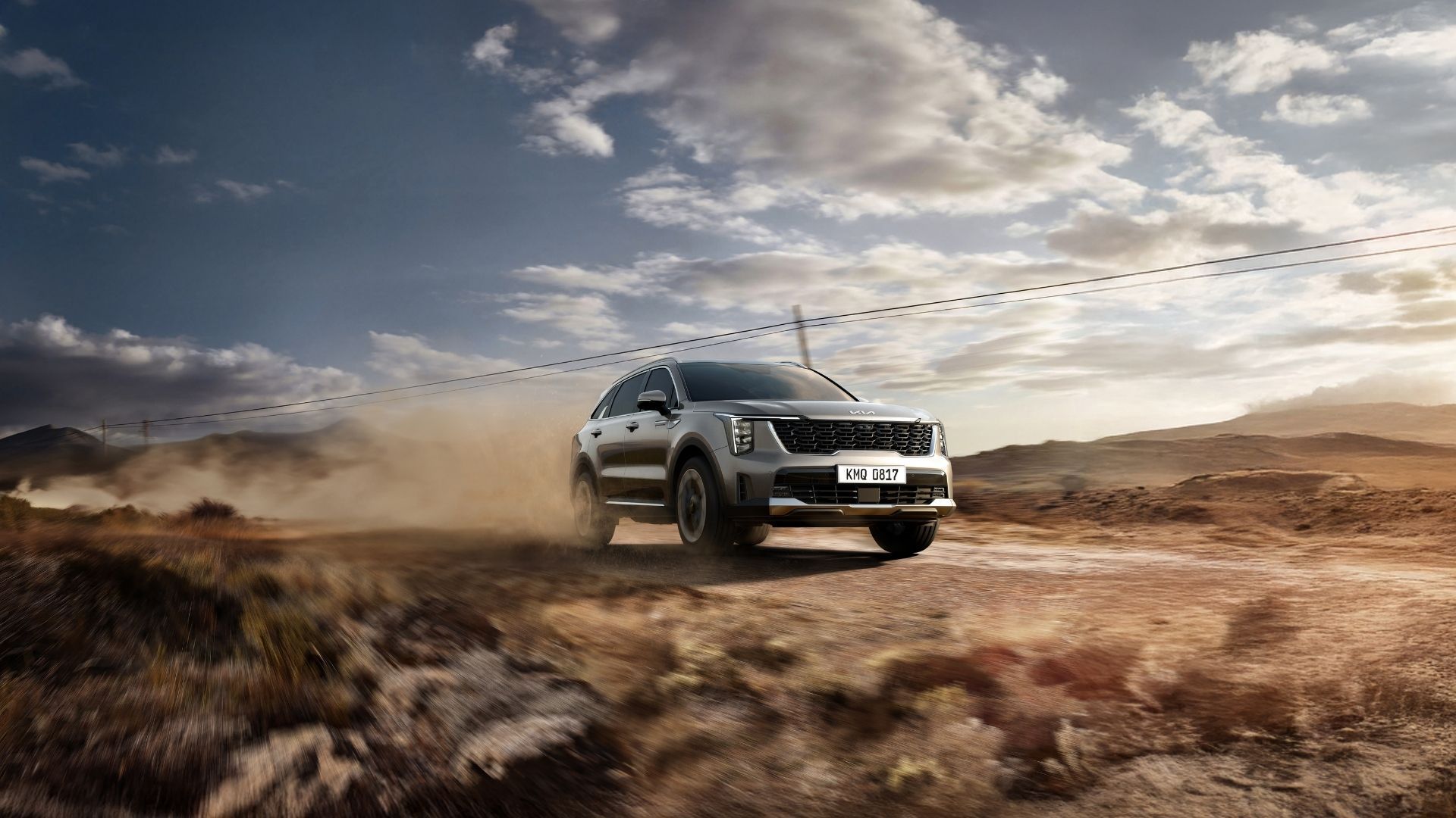 Silver SUV driving through a dusty desert landscape under a cloudy sky