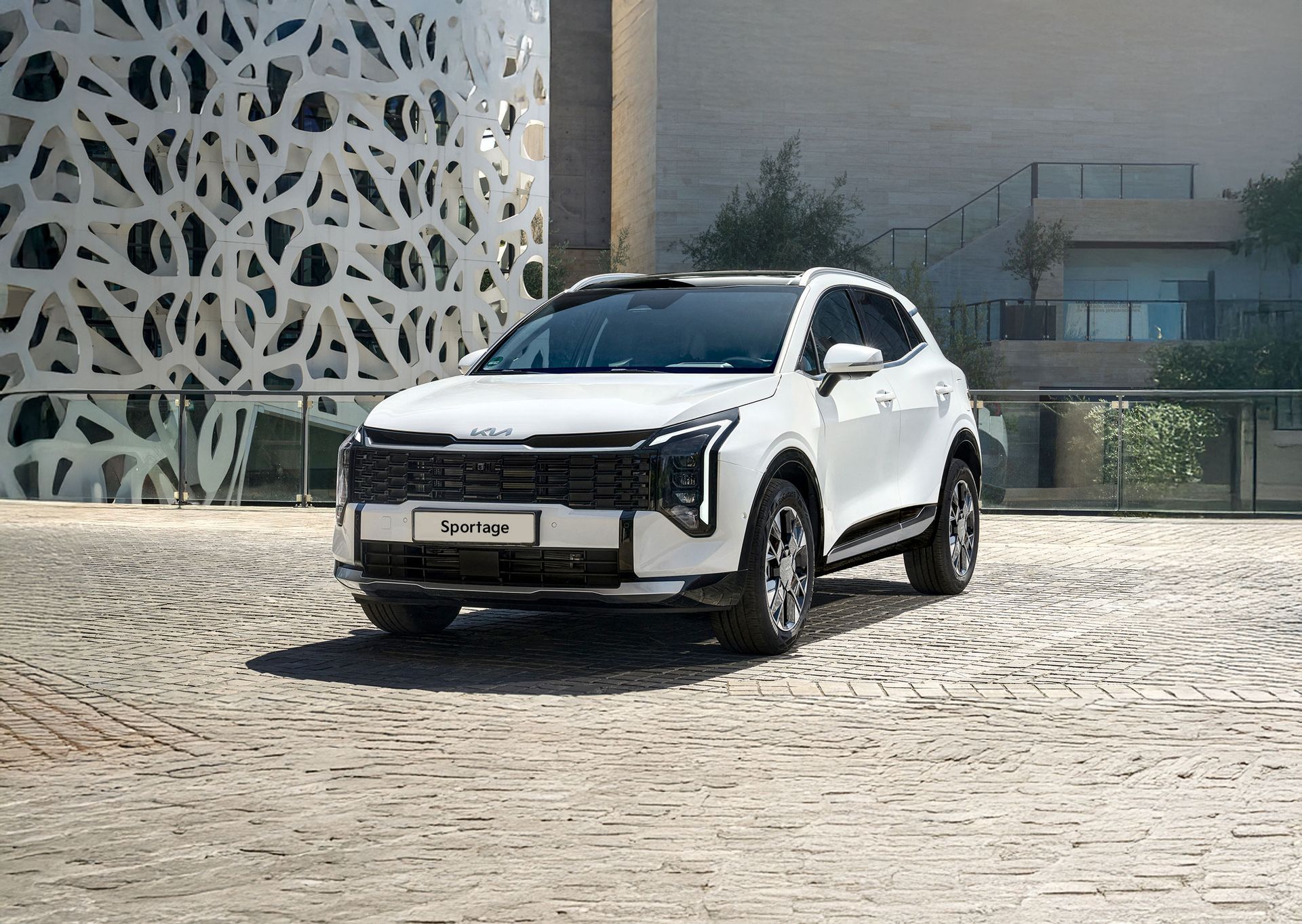 White SUV parked on a cobblestone driveway beside a patterned wall and modern building.