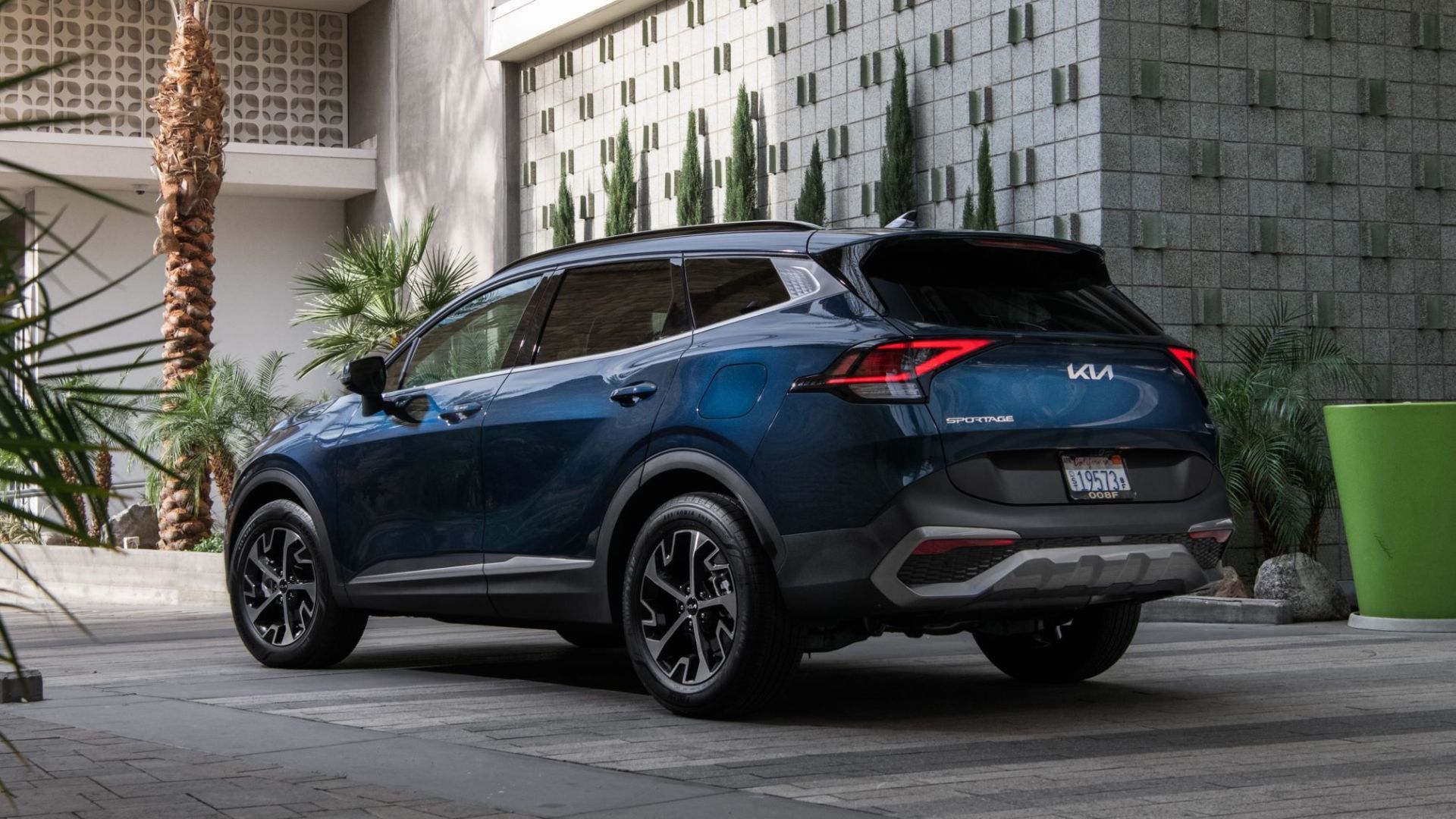 Blue SUV parked beside a modern building with green planter and tiled wall