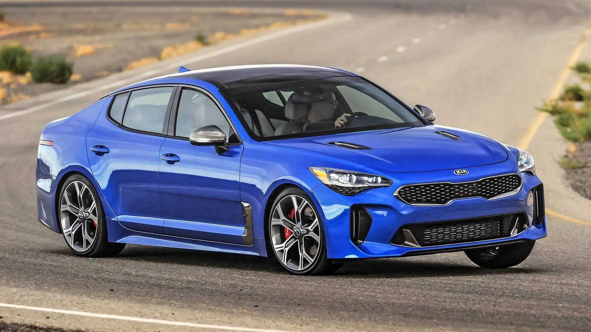 Blue sports sedan driving on a road, angled toward the camera in a desert setting