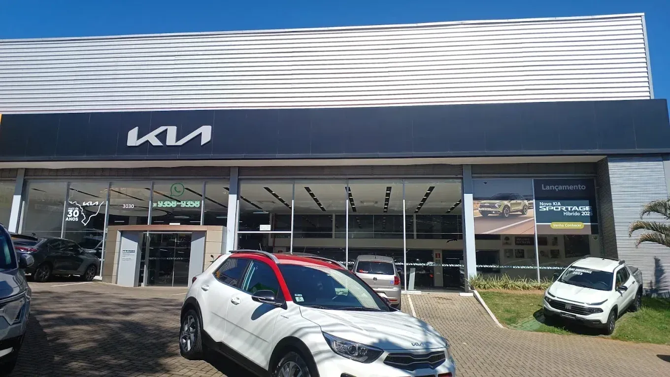 Kia car dealership storefront with several parked cars outside, including a white SUV in front.