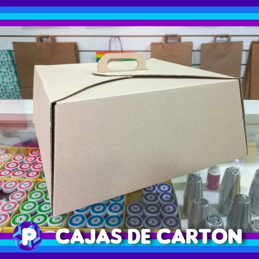 Caja de cartón color crema con asa sobre una mesa de colores y estampada, con materiales para manualidades al fondo
