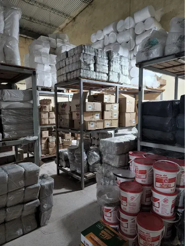 Trastero con cajas apiladas, rollos envueltos y cubos rojos y blancos en estanterías metálicas