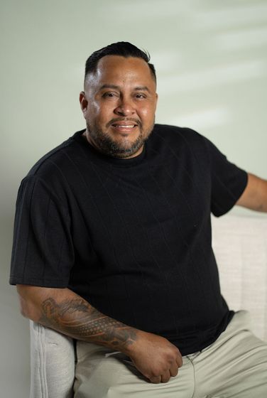Portrait of a man in a black polo shirt standing against a dark background.
