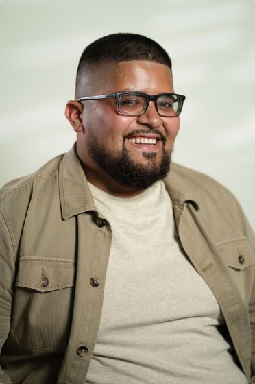 Smiling man in glasses wearing a black polo shirt against a dark background