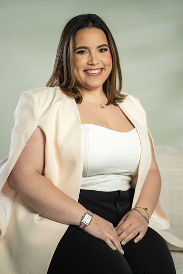 Smiling woman in a black blazer posing against a dark background.