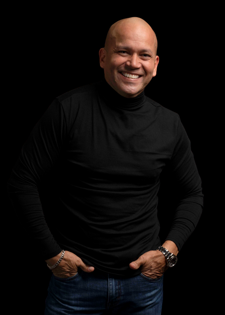Smiling bald man in a black turtleneck and jeans against a dark background