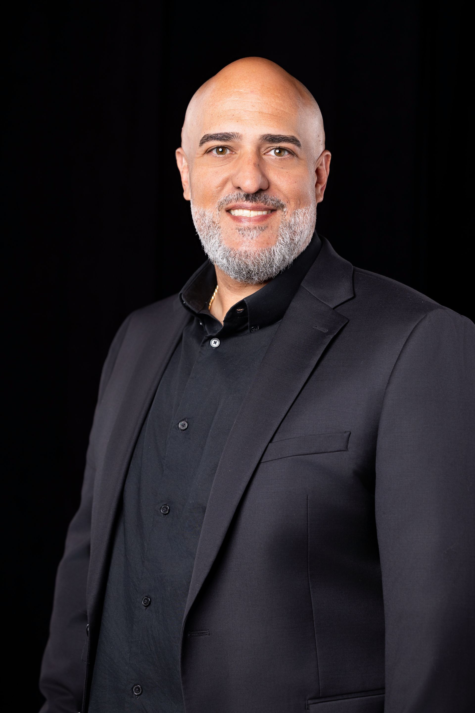Smiling bald man in a black suit and shirt against a dark background