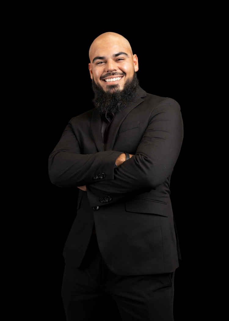 Smiling person in a black suit with arms crossed against a dark background
