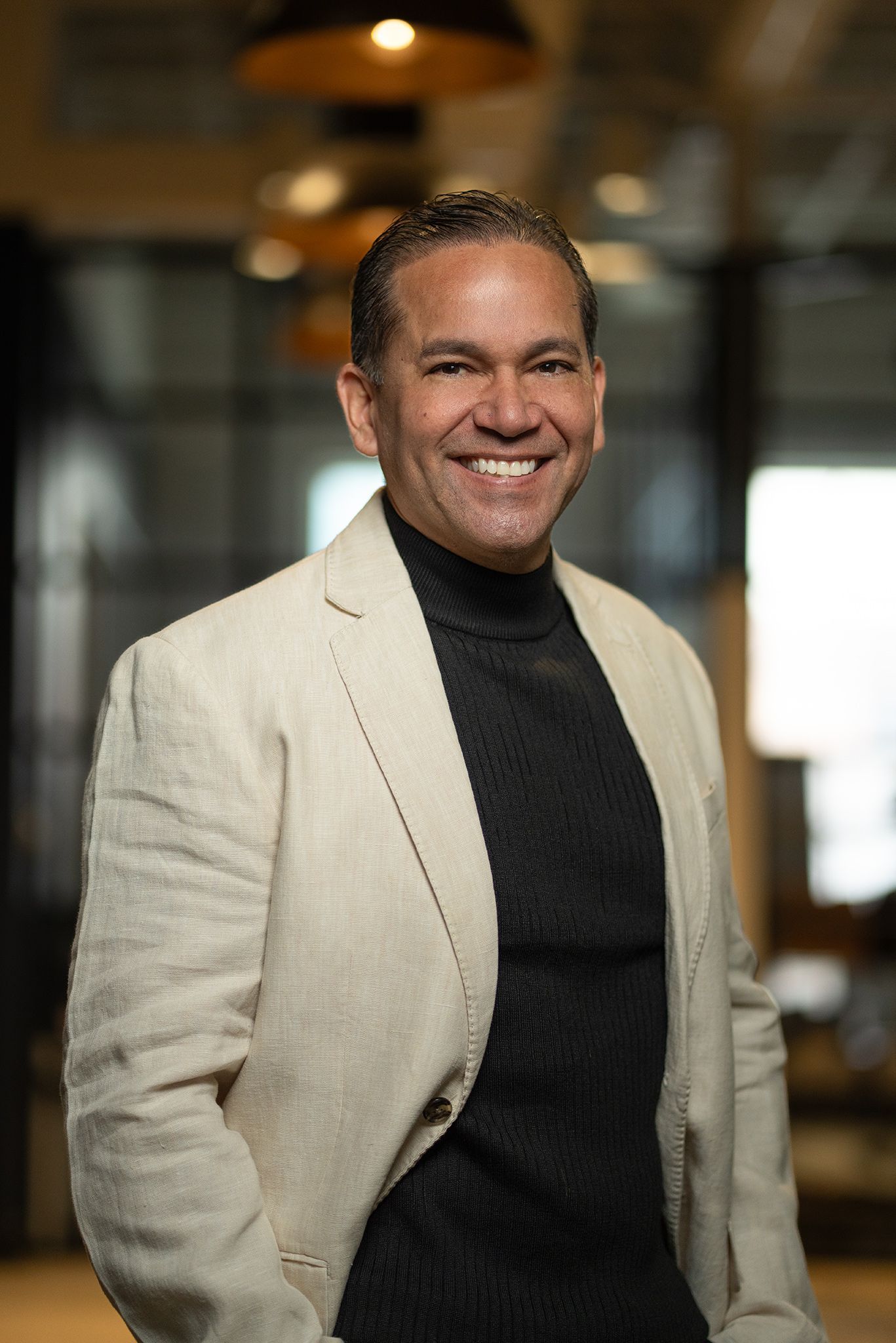 Smiling bald man in a black turtleneck and jeans against a black background