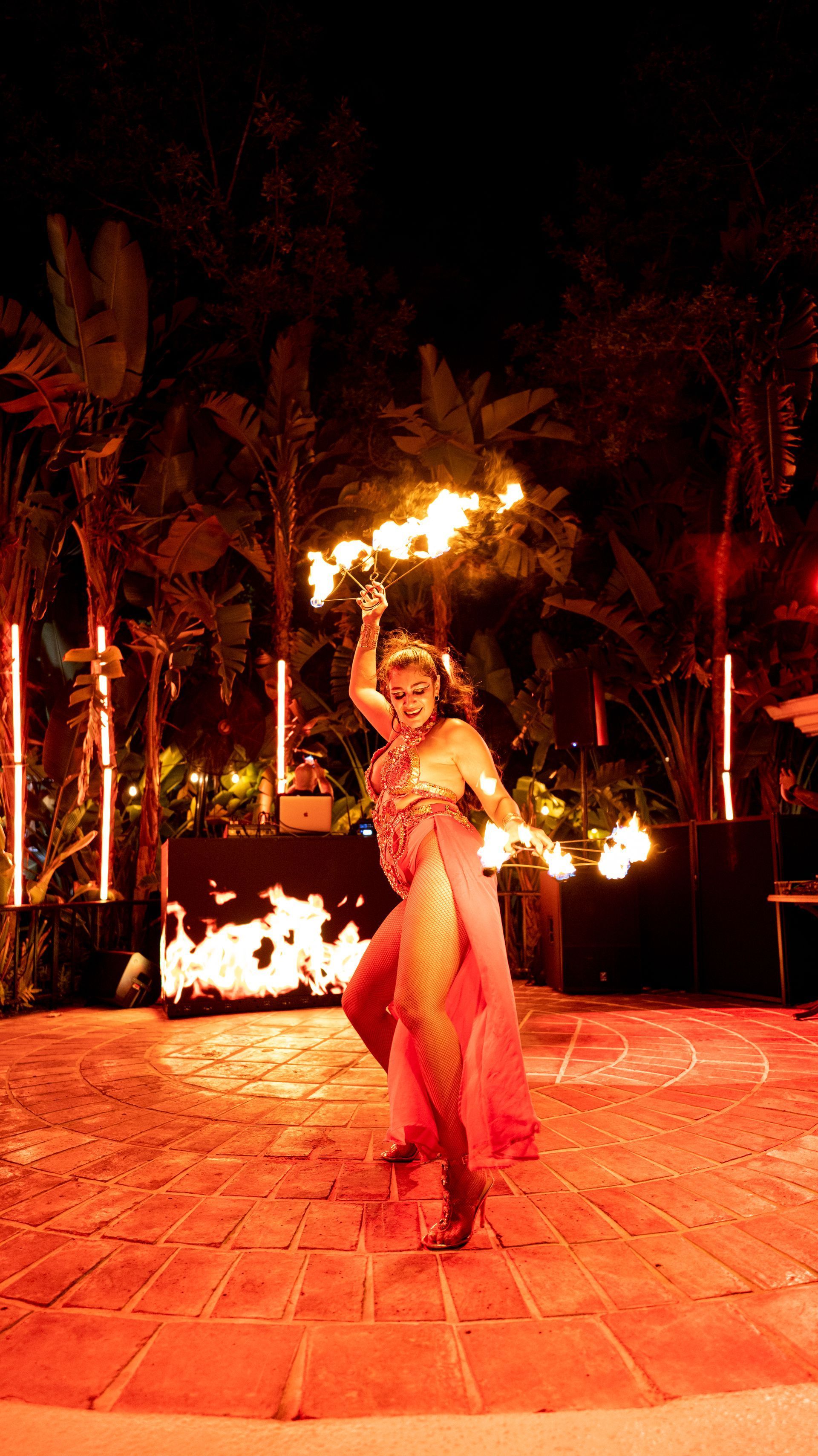 Fire dancer performing with flames in a palm-lined outdoor courtyard at night