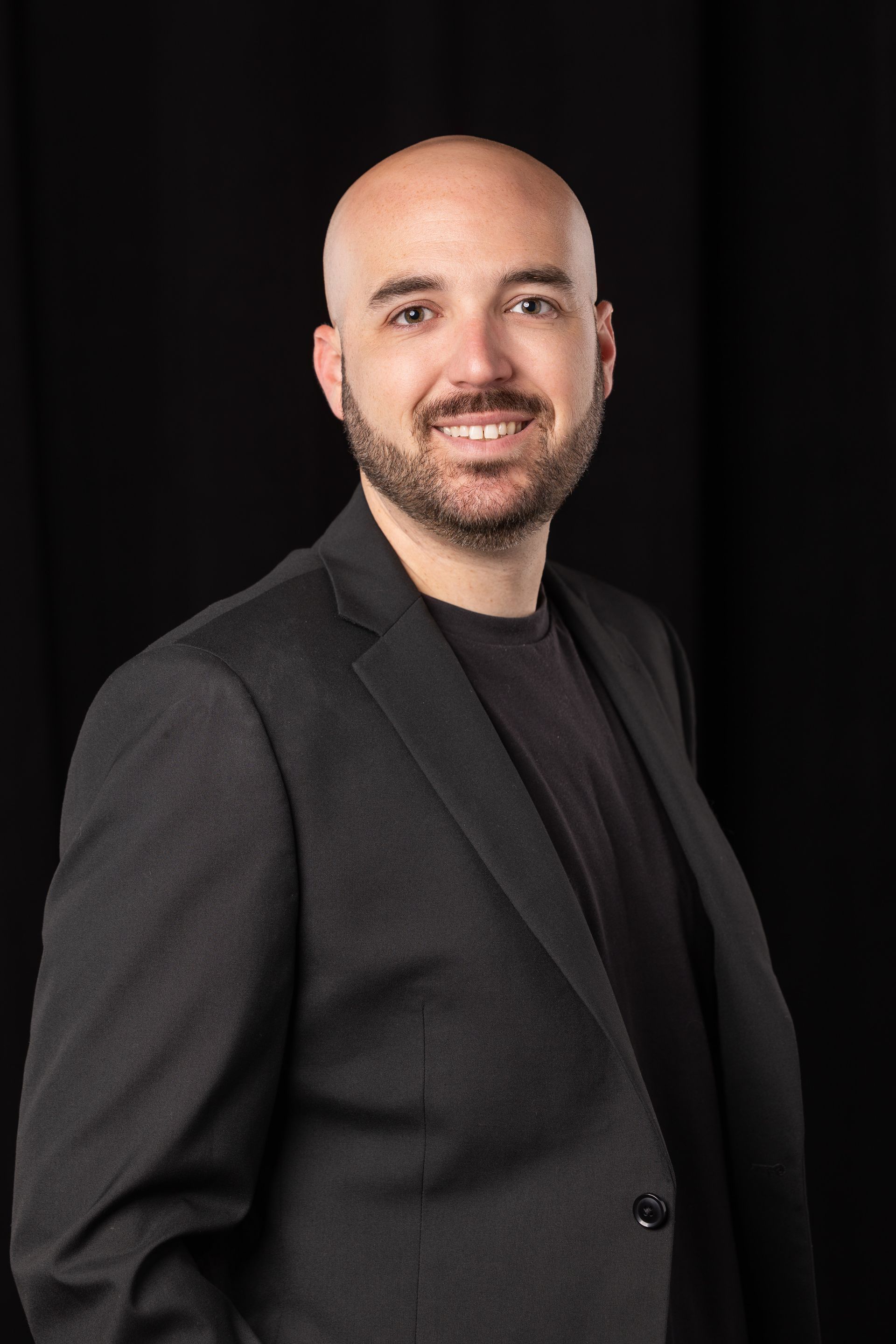 Smiling bald man in a dark blazer and shirt against a black background