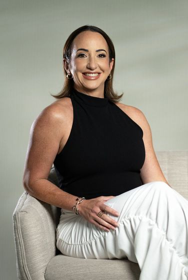 Smiling woman in a black outfit standing against a dark studio backdrop