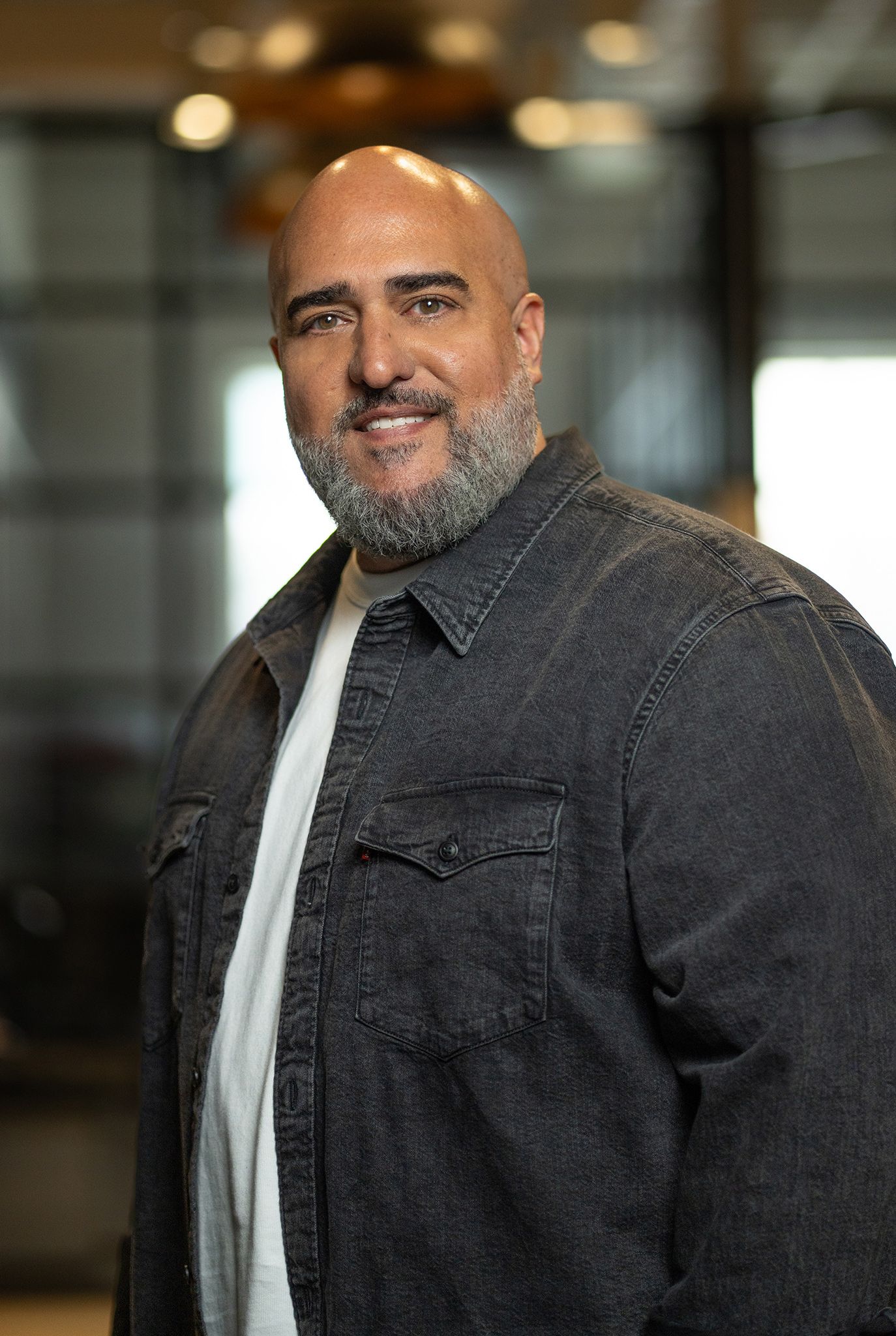 Smiling bald man in a black suit and shirt against a dark background