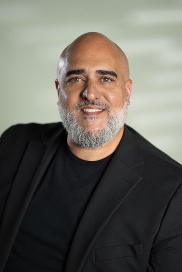 Smiling bald man in a black suit and shirt against a black background