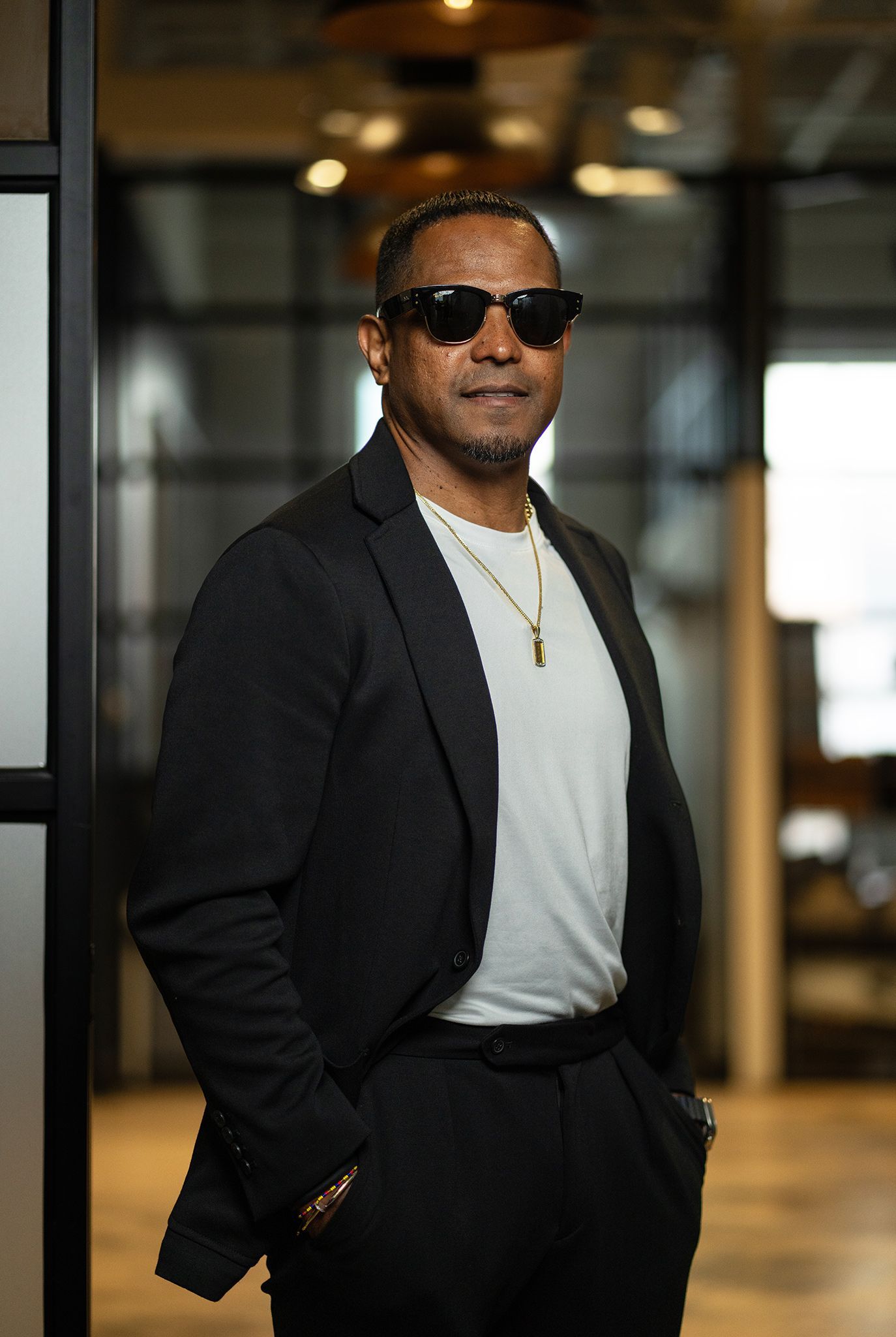 Man in a dark suit and white shirt standing against a black backdrop, smiling at the camera.